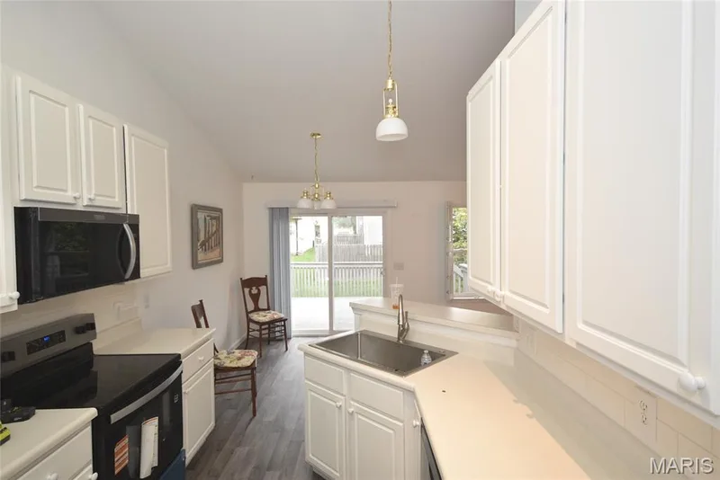 Vaulted ceiling kitchen featuring white cabinetry, a stainless steel sink, light-toned countertops, and wood-finish flooring — 1129 Piepers Glen Lane #8A, O'Fallon, MO 63366