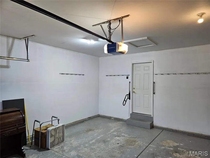 Interior garage space featuring a concrete floor, overhead lighting, and an access door — 1129 Piepers Glen Lane #8A, O'Fallon, MO 63366
