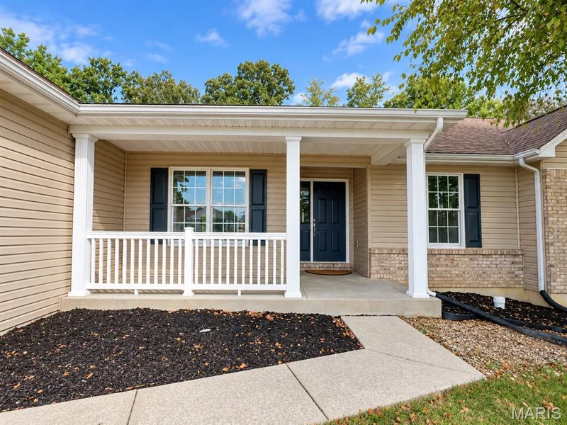 Welcoming front porch with white railing, tan siding, dark blue front door, and brick accents — 1731 Fairview Farms Circle, Wentzville, MO 63385