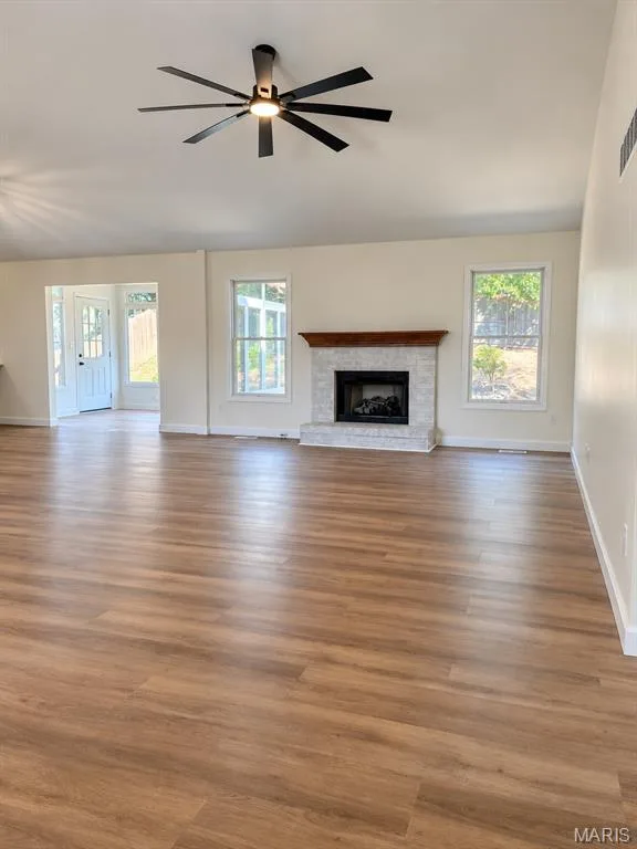 Spacious interior featuring wood-finish flooring, a contemporary ceiling fan, and a fireplace with a stone surround and wood mantel — 1731 Fairview Farms Circle, Wentzville, MO 63385