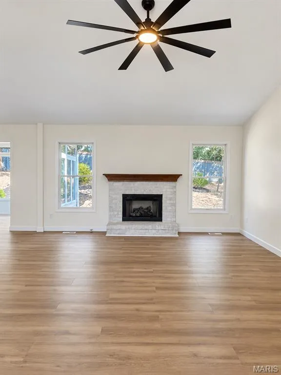 Spacious room featuring wood-finish flooring, a contemporary ceiling fan, and a fireplace with a white stone surround and wood mantel — 1731 Fairview Farms Circle, Wentzville, MO 63385