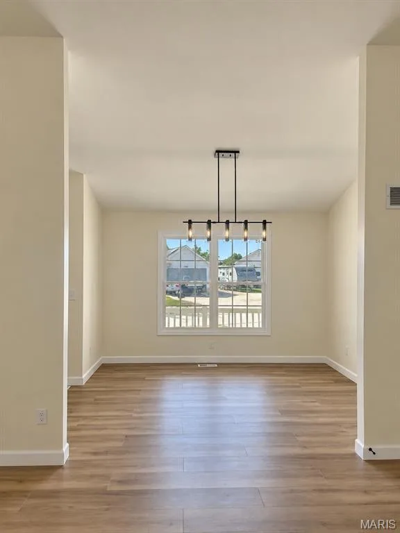 Expansive room featuring wood-finish flooring, a large window with white trim, and a contemporary linear chandelier with a matte black finish — 1731 Fairview Farms Circle, Wentzville, MO 63385