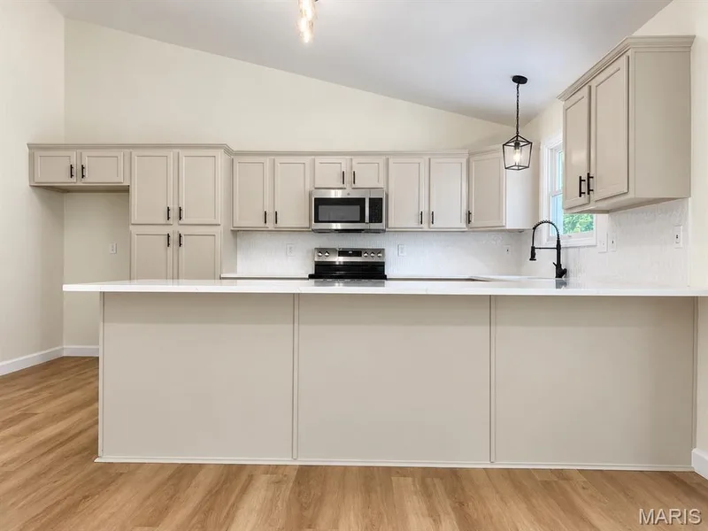 Modern kitchen featuring wood-finish flooring, vaulted ceiling, white quartz countertops, full suite of stainless steel appliances, and a tile backsplash — 1731 Fairview Farms Circle, Wentzville, MO 63385