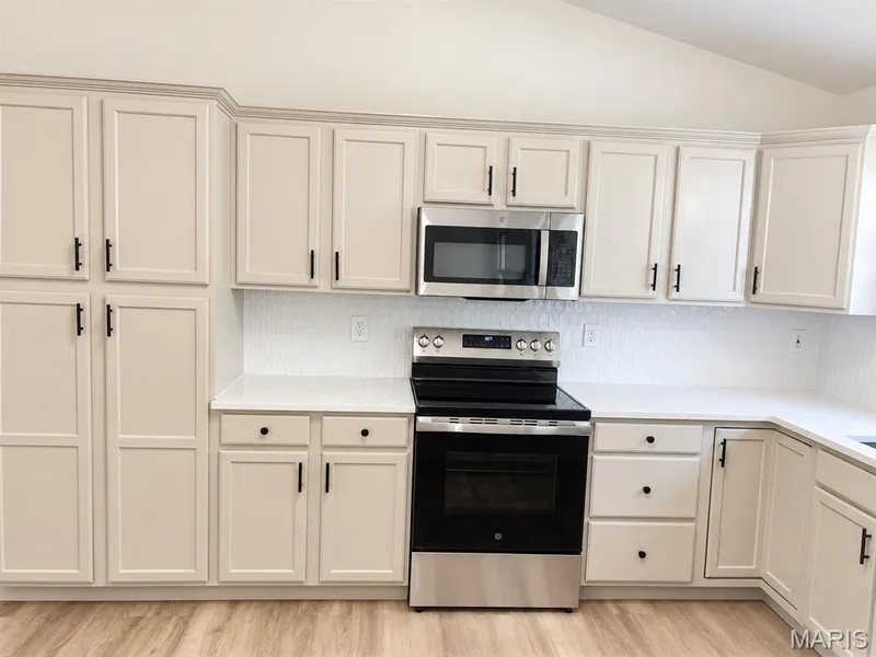 Extensive cabinetry with modern black hardware, stainless steel appliances, white countertops, and a full-height backsplash — 1731 Fairview Farms Circle, Wentzville, MO 63385