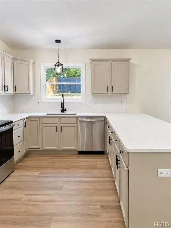 U-shaped kitchen with light-toned cabinetry, stainless steel dishwasher, white countertops, wood-finish flooring, and a single basin sink with a matte black faucet — 1731 Fairview Farms Circle, Wentzville, MO 63385
