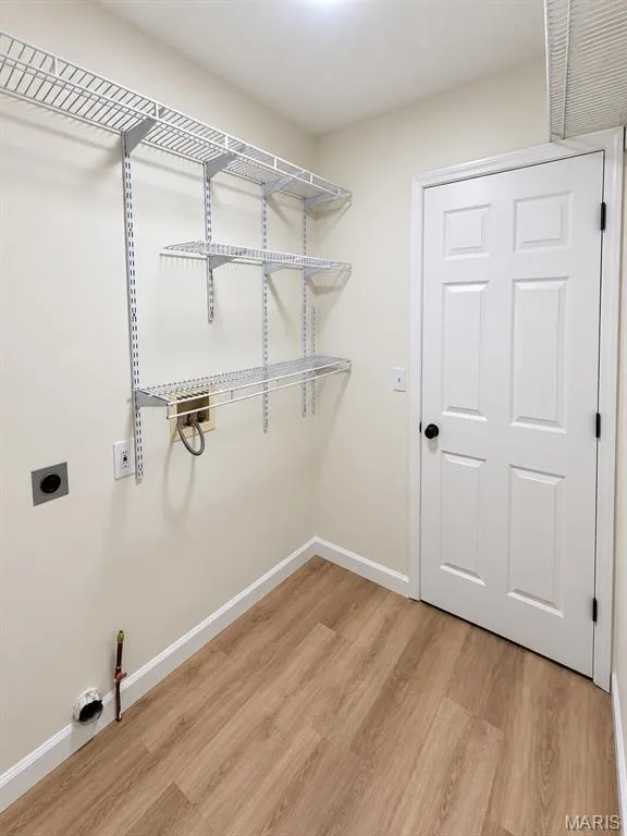 Utility area featuring multi-tiered wire shelving, wood-finish flooring, and a panel door — 1731 Fairview Farms Circle, Wentzville, MO 63385