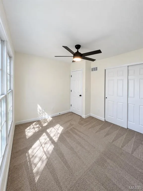 Neutral tone carpet flooring, multiple panel windows, ceiling-mounted fan with integrated lighting, and white sliding closet doors — 1731 Fairview Farms Circle, Wentzville, MO 63385