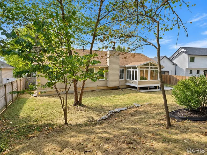 Rear exterior featuring a sunroom, deck, wood fencing, and mature trees — 1731 Fairview Farms Circle, Wentzville, MO 63385