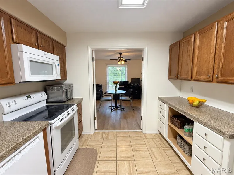 Kitchen featuring wood cabinetry, white appliances, speckled countertops, and tiled flooring — 15631 Hedgeford Court #9, Chesterfield, MO 63017
