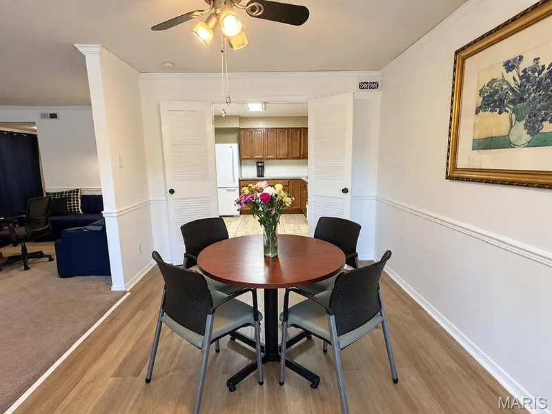 Dining area featuring wood-finish flooring, wainscoting, a ceiling fan with integrated lighting, and louvered double doors — 15631 Hedgeford Court #9, Chesterfield, MO 63017