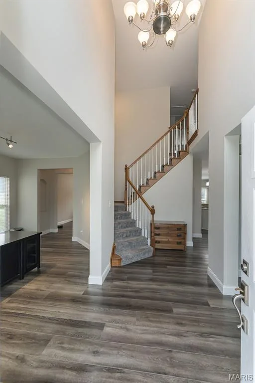 Two-story entryway with a decorative chandelier, wood-finish flooring, and a carpeted staircase with a wood handrail and white balusters — 472 Brookhaven Court, O'Fallon, MO 63368