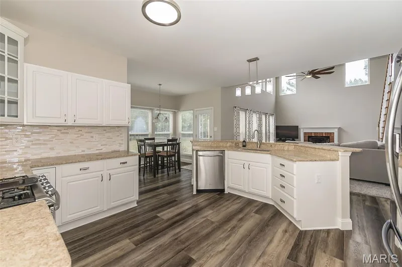 Chef's kitchen featuring white cabinetry with brushed nickel hardware, quartz countertops, subway tile backsplash, stainless steel appliances including a gas cooktop and dishwasher, and wood-finish flooring throughout the open concept space with recessed and pendant lighting — 472 Brookhaven Court, O'Fallon, MO 63368