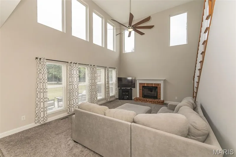 Vaulted ceiling with a wood-finish ceiling fan, multiple upper-level windows, and a brick fireplace featuring a white mantel — 472 Brookhaven Court, O'Fallon, MO 63368