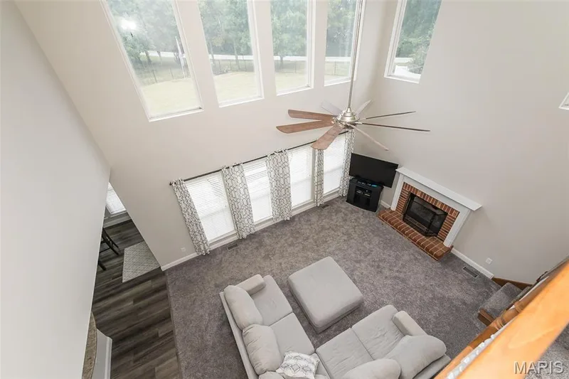 Vaulted ceiling with multiple windows and a ceiling fan, brick fireplace with a white mantel, and wood-finish flooring in an adjoining space — 472 Brookhaven Court, O'Fallon, MO 63368