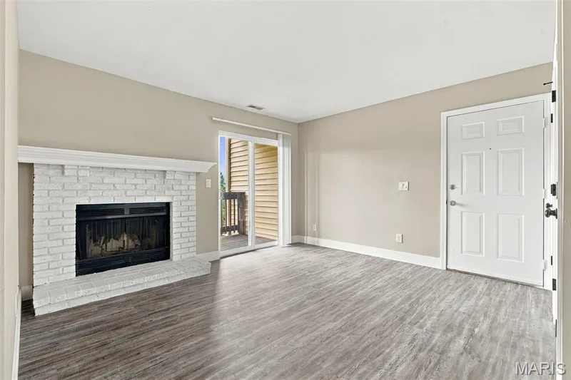 LVP flooring, white brick fireplace with mantel, sliding glass door with balcony access, and a multi-panel entry door — 2415 Sandalwood Creek Court #C, Wildwood, MO 63038