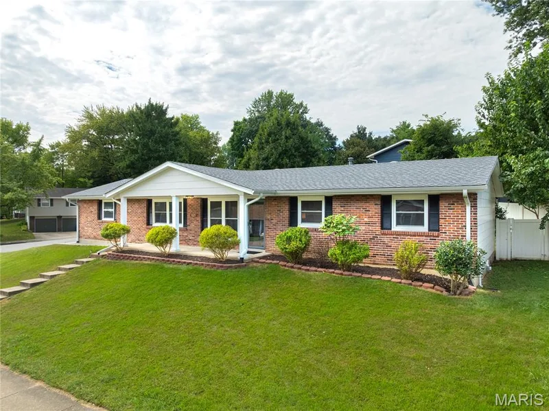 Brick exterior residence with a covered porch entry, foundational landscaping, and a sloped lawn — 3025 Sherwood Lane, St Charles, MO 63301