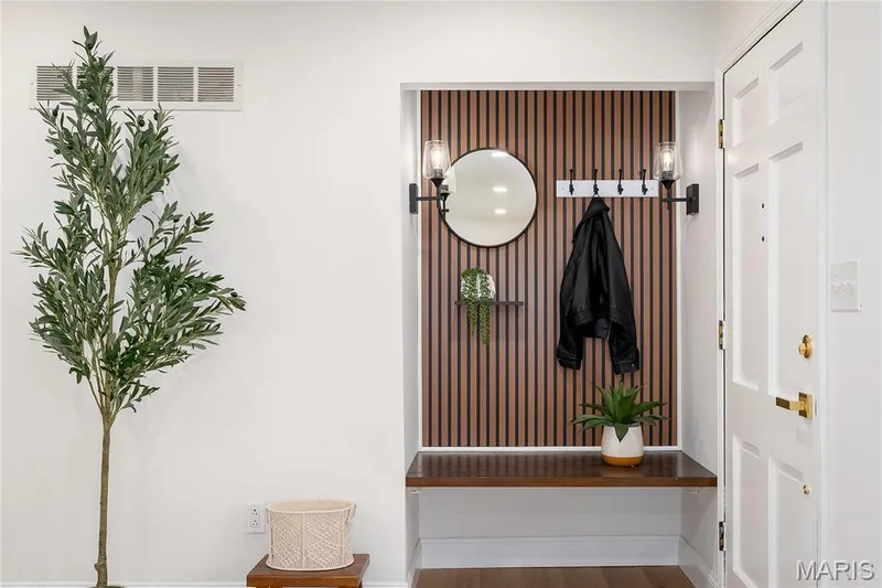 Entryway featuring a built-in bench, wood slat accent wall, integrated coat rack, and a round wall mirror — 3025 Sherwood Lane, St Charles, MO 63301