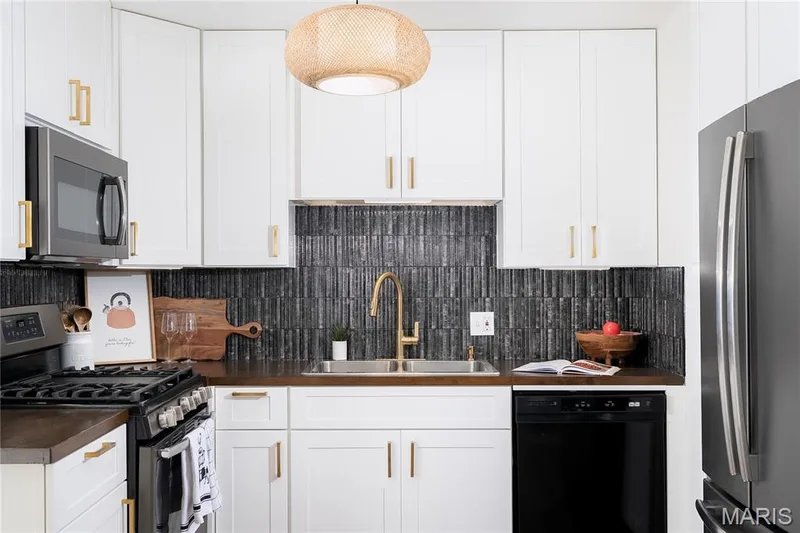 Kitchen featuring white cabinetry with gold-finish hardware, dark vertical tile backsplash, dark countertops, and stainless steel appliances — 3025 Sherwood Lane, St Charles, MO 63301