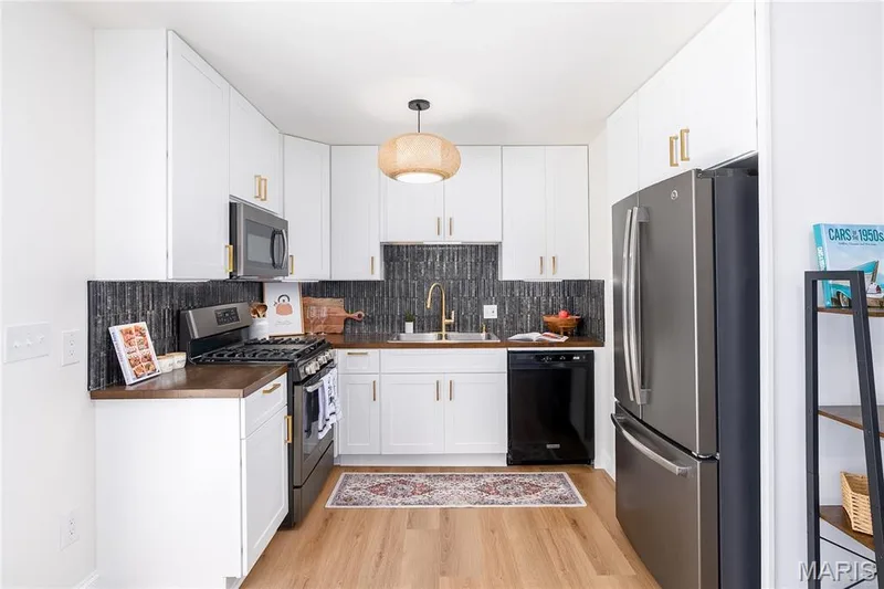 White cabinetry with gold-finish hardware, dark backsplash, stainless steel appliances, and wood-finish flooring — 3025 Sherwood Lane, St Charles, MO 63301