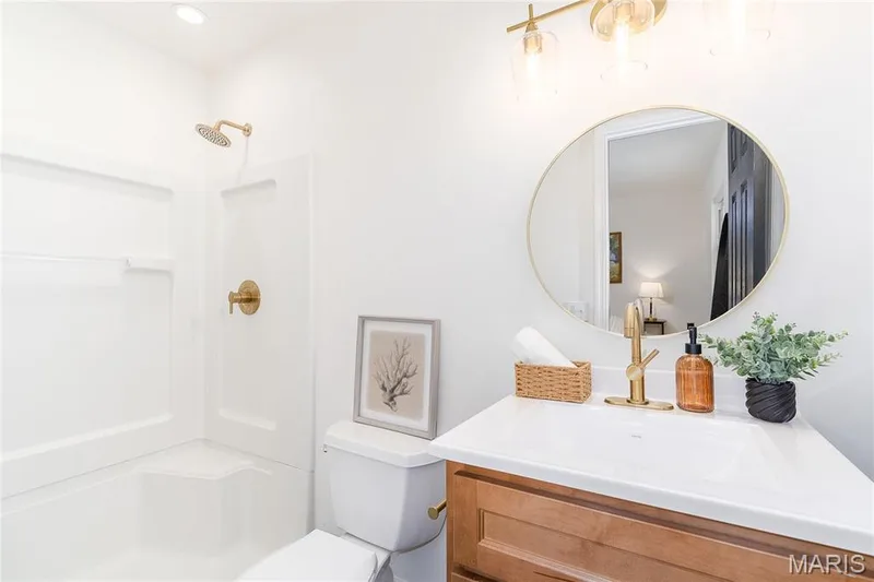 White shower enclosure with brass fixtures, single vanity with light wood-finish cabinetry, white countertop, and round wall-mounted mirror — 3025 Sherwood Lane, St Charles, MO 63301