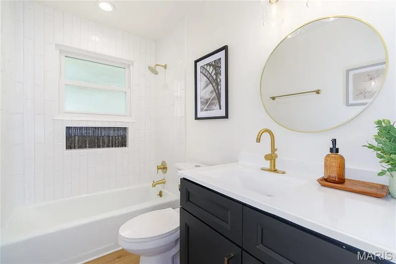 White subway tile shower surround with a built-in niche, gold-finish fixtures, a window, and a dark vanity with a white countertop — 3025 Sherwood Lane, St Charles, MO 63301