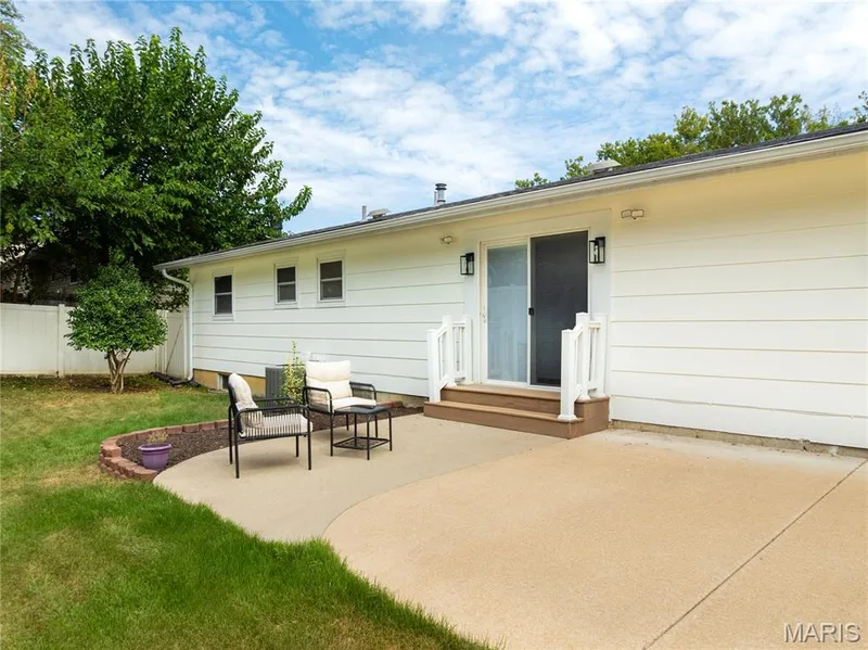 Expansive concrete patio with direct access to a sliding glass door, featuring a white vinyl fence and mature trees — 3025 Sherwood Lane, St Charles, MO 63301