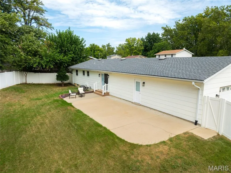 Expansive backyard featuring a concrete patio, mature landscaping, white privacy fencing, and a newly installed roofing system — 3025 Sherwood Lane, St Charles, MO 63301