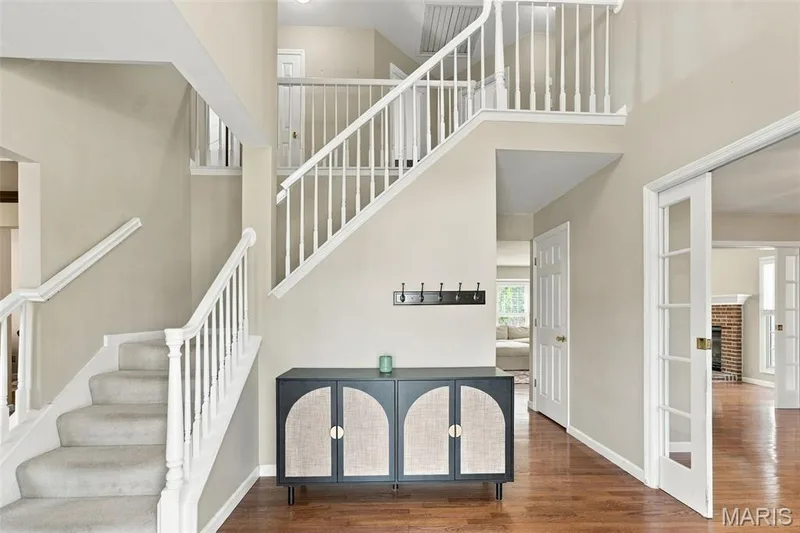 Two-story foyer featuring wood-finish flooring, white spindle staircase, and French doors — 8 Jacobs Place Court, O'Fallon, MO 63376
