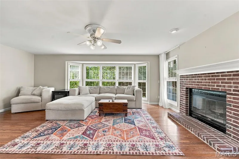 Hardwood flooring, brick fireplace with mantel, bay window, recessed lighting, and ceiling fan — 8 Jacobs Place Court, O'Fallon, MO 63376