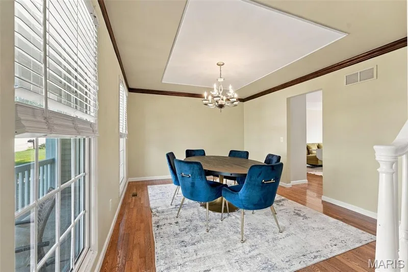 Recessed ceiling panel with a chandelier, wood-finish flooring, two large windows, and white painted balusters — 8 Jacobs Place Court, O'Fallon, MO 63376