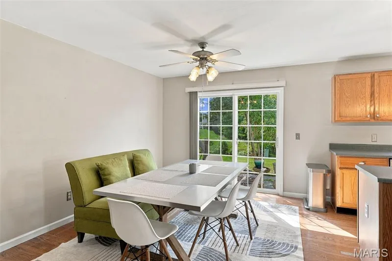 Wood-finish flooring, sliding glass door, overhead ceiling fan with light fixture, wood cabinetry, and dark countertops — 8 Jacobs Place Court, O'Fallon, MO 63376