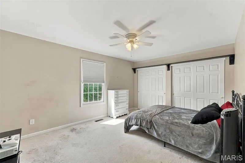 Window with white blinds, neutral wall tones, white multi-panel doors, ceiling fan with integrated lighting, and light-colored carpeting — 8 Jacobs Place Court, O'Fallon, MO 63376