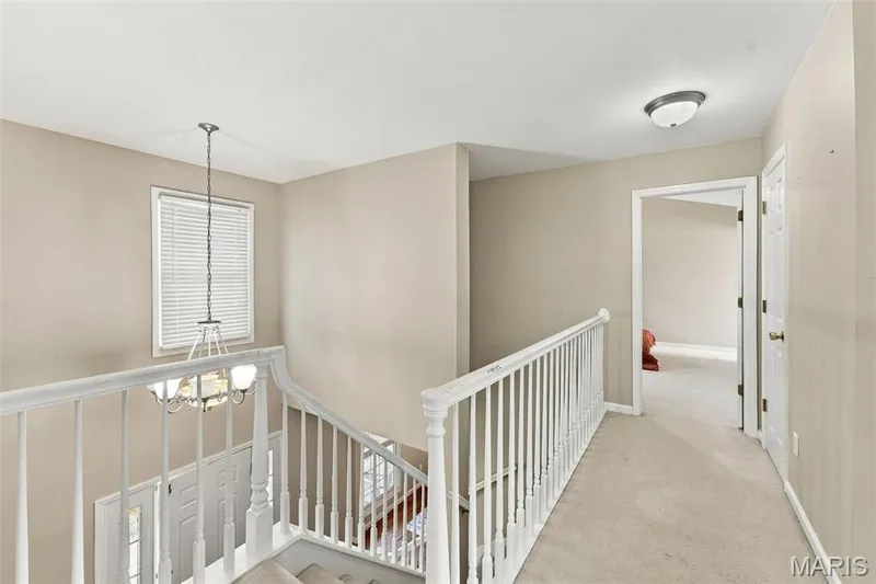 Upper-level hallway featuring neutral wall paint, carpet flooring, a window with blinds, and white baluster railing — 8 Jacobs Place Court, O'Fallon, MO 63376