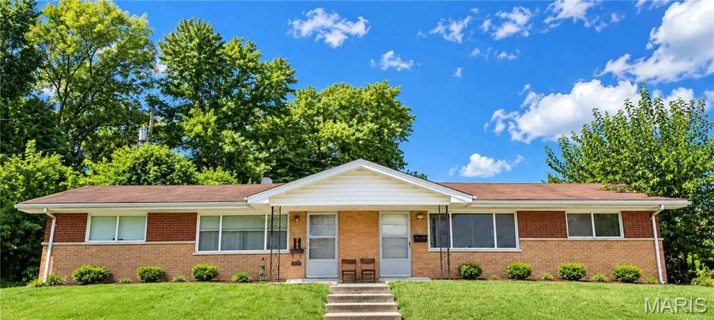Brick exterior with a gabled entry, featuring a concrete walkway and front steps, and a grassy front yard with foundational shrubbery — 417-419 S Cadillac Drive, St Charles, MO 63301
