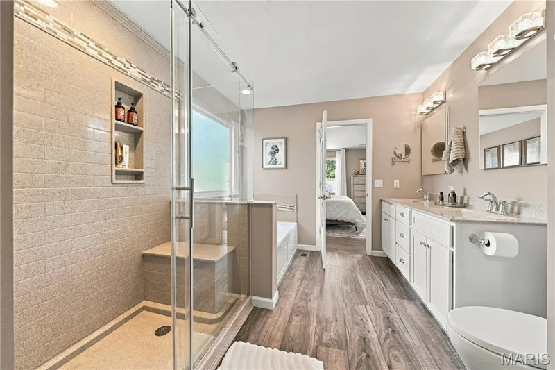 Privacy-glass window, luxury vinyl plank flooring, white shaker cabinetry, double vanity with medicine cabinets above, stylish wall lighting and neutral decor. — 1417 Plantation Manor Court, St Peters, MO 63303