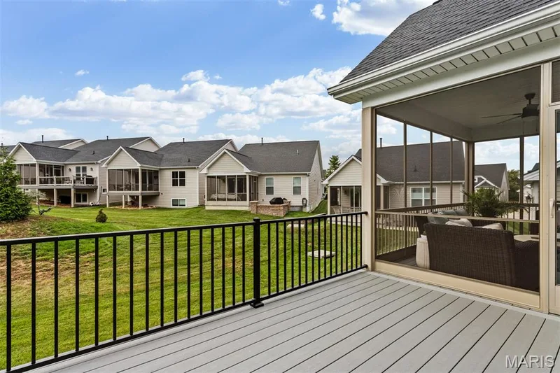 Outdoor living space featuring a screened porch with a ceiling fan, a composite deck, and a black metal railing overlooking a sloped lawn — 17028 Fire Glow Drive, Ballwin, MO 63011