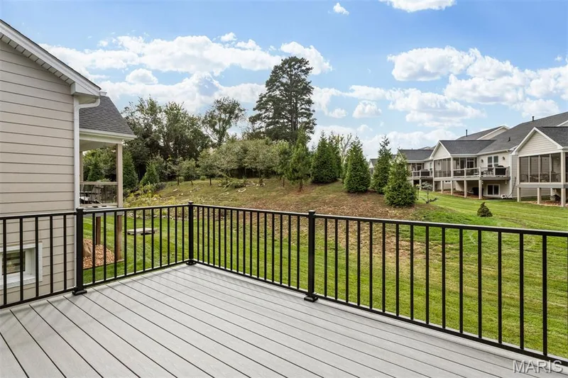 Expansive outdoor deck with composite decking and black metal railings, overlooking a landscaped grassy area with mature trees — 17028 Fire Glow Drive, Ballwin, MO 63011