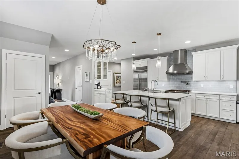 Open-concept kitchen and dining area featuring wood-finish flooring, white cabinetry, a large kitchen island with seating, stainless steel appliances, and a tiled backsplash — 17028 Fire Glow Drive, Ballwin, MO 63011