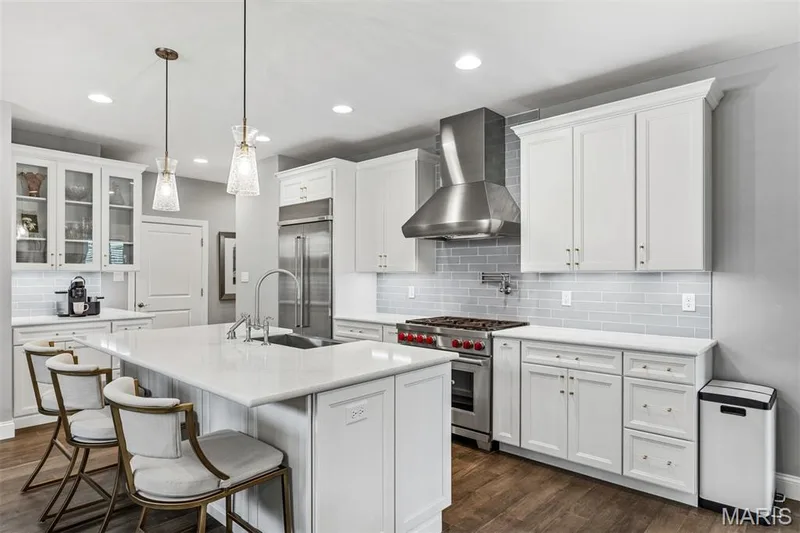 Spacious kitchen featuring an expansive central island, white cabinetry, integrated stainless steel appliances, a subway tile backsplash, and wood-finish flooring — 17028 Fire Glow Drive, Ballwin, MO 63011