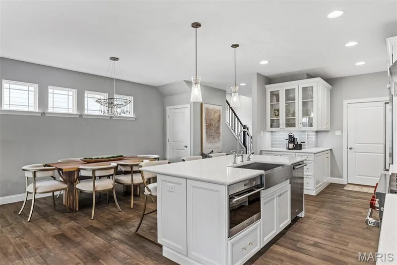 Kitchen island with an undermount sink, pendant lighting, shaker-style cabinetry, wood-finish flooring, and a subway tile backsplash — 17028 Fire Glow Drive, Ballwin, MO 63011