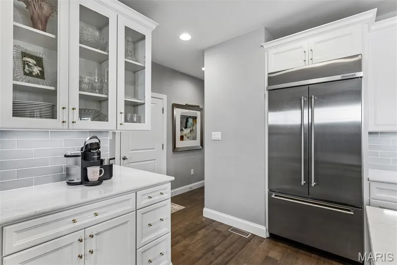 White shaker-style cabinetry with glass-front uppers, white countertop, light grey subway tile backsplash, and stainless steel French door refrigerator — 17028 Fire Glow Drive, Ballwin, MO 63011
