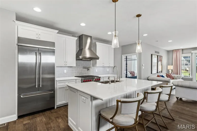 Gourmet kitchen with stainless steel appliances, white cabinetry, a subway tile backsplash, and an expansive island with a sink — 17028 Fire Glow Drive, Ballwin, MO 63011