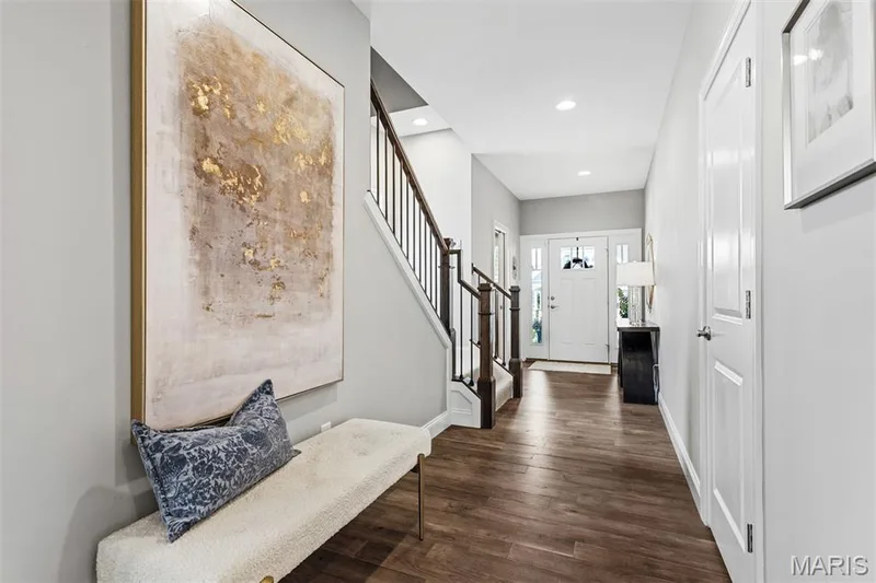 Entryway featuring wood-finish flooring, a white front door with decorative glass, and a staircase with dark wood railings — 17028 Fire Glow Drive, Ballwin, MO 63011