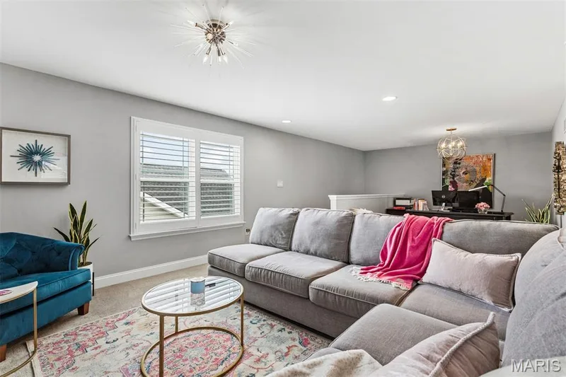 Sophisticated living room featuring a spacious sectional sofa, polished concrete flooring, and a round brass-accented coffee table — 17028 Fire Glow Drive, Ballwin, MO 63011