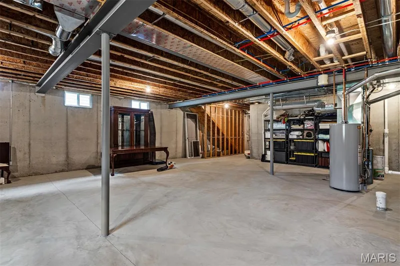 Unfinished basement featuring concrete flooring, exposed ceiling joists, and a hot water heater — 17028 Fire Glow Drive, Ballwin, MO 63011