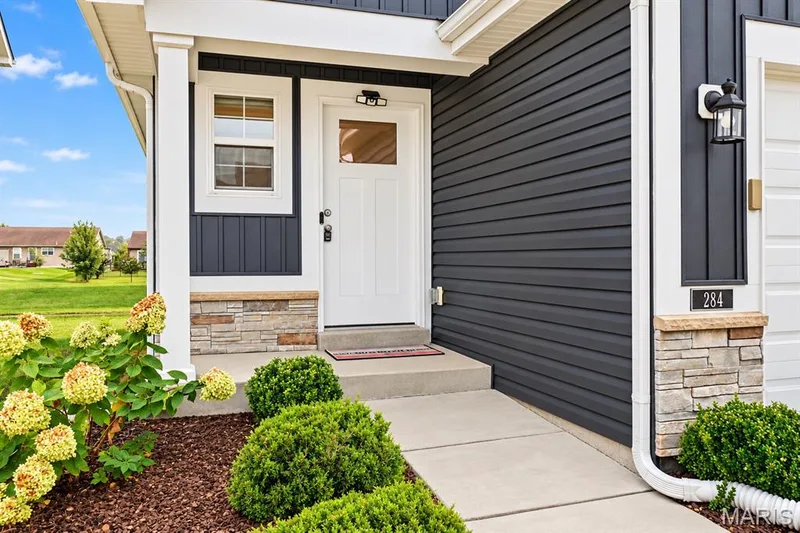 Exterior featuring dark horizontal siding, white trim, stone veneer accents, and a concrete pathway — 284 Crestfield Court, St Charles, MO 63301