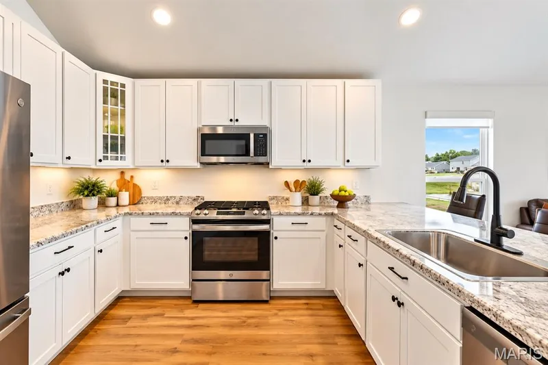 Kitchen featuring white cabinetry, stainless steel appliances, speckled countertops, wood-finish flooring, and a large window — 284 Crestfield Court, St Charles, MO 63301