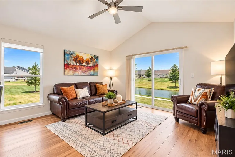 Vaulted ceiling with a ceiling fan, wood-finish flooring, large window, and sliding glass doors revealing a waterfront backdrop — 284 Crestfield Court, St Charles, MO 63301