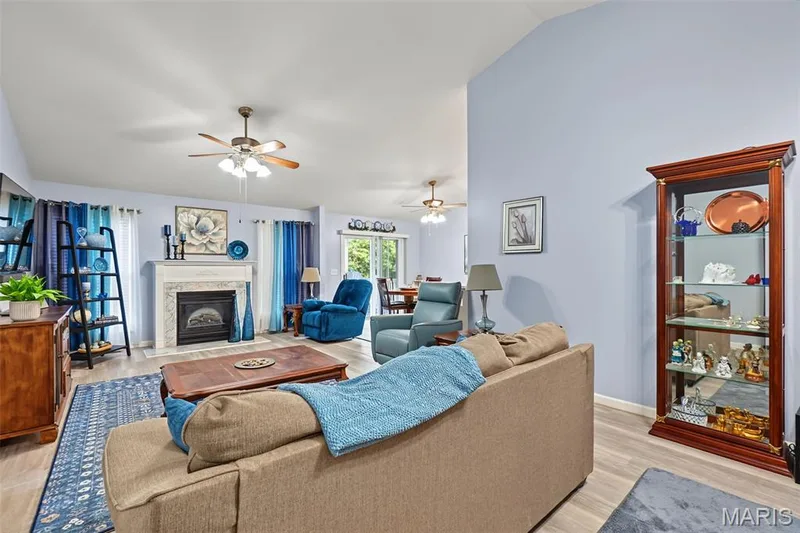 Vaulted ceilings accent this living space featuring wood-finish flooring, a fireplace with a stone surround, and a ceiling fan — 8 Soenker Circle, St Peters, MO 63376
