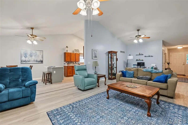 Vaulted ceiling with multiple ceiling fans, light wood-finish flooring, and a kitchen featuring wood cabinetry and a tile backsplash — 8 Soenker Circle, St Peters, MO 63376